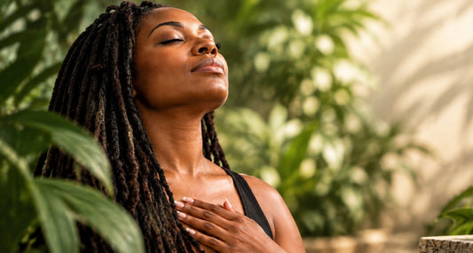 Woman with locs practicing mindful breathing outdoors surrounded by tropical plants and white flowers — Root & Remedy wellness